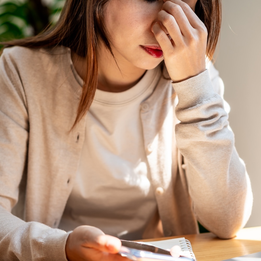Tired and stressed young Asian woman sitting at her working place with a cup of coffee and breakfast in the morning
